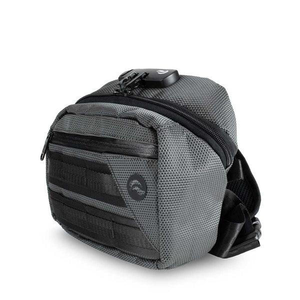 The Skunk Kross Stash Storage Bag by Skunk is a small, gray, textured shoulder bag with black zippers, a front pocket, carbon lining for odor-proof storage, and a combo lock. It features a black strap and is shown on a white background.